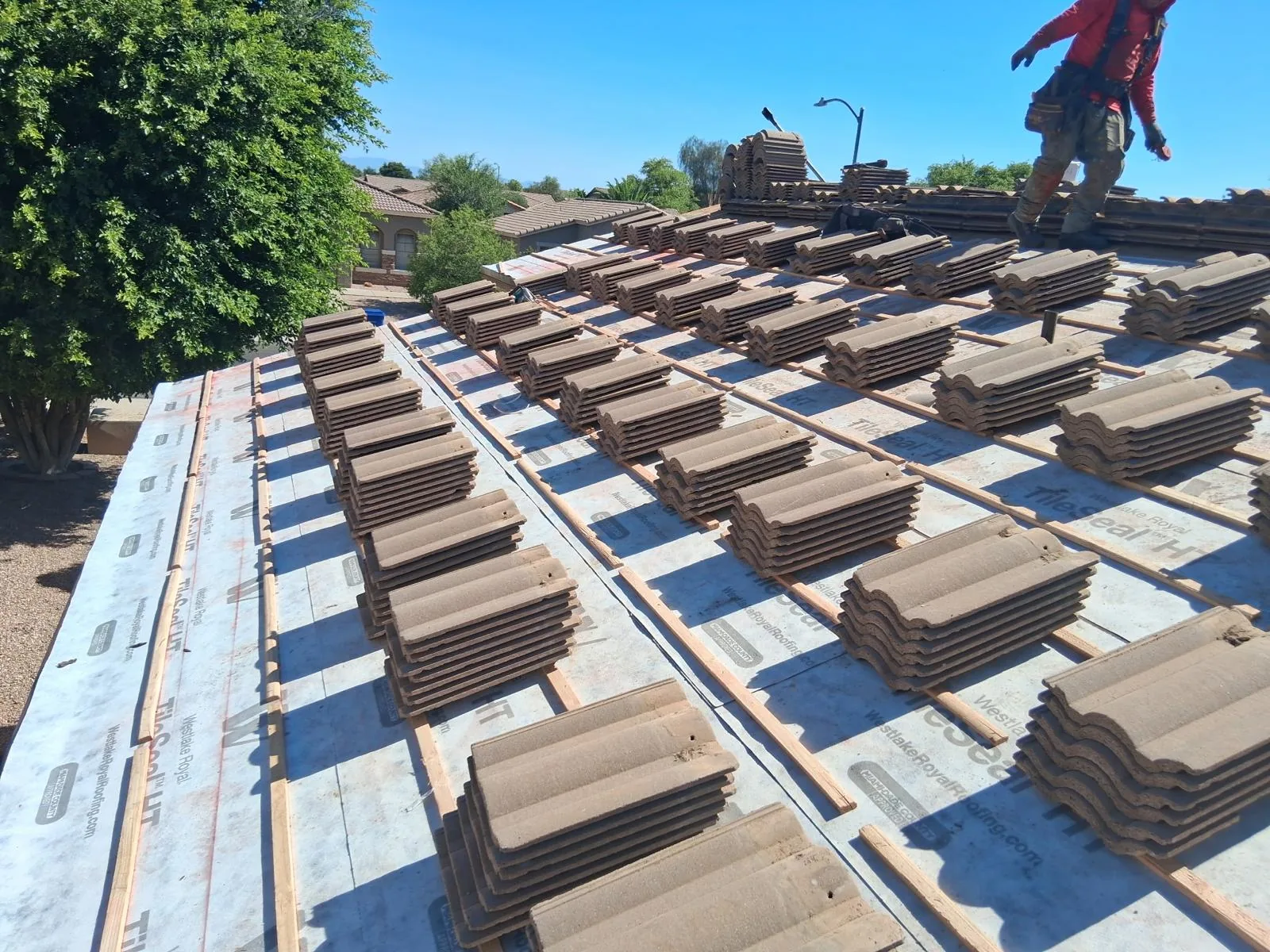 Concrete S-tile stacked in rows over fresh underlayment and battens, ready to be set — crew member walking the ridge.