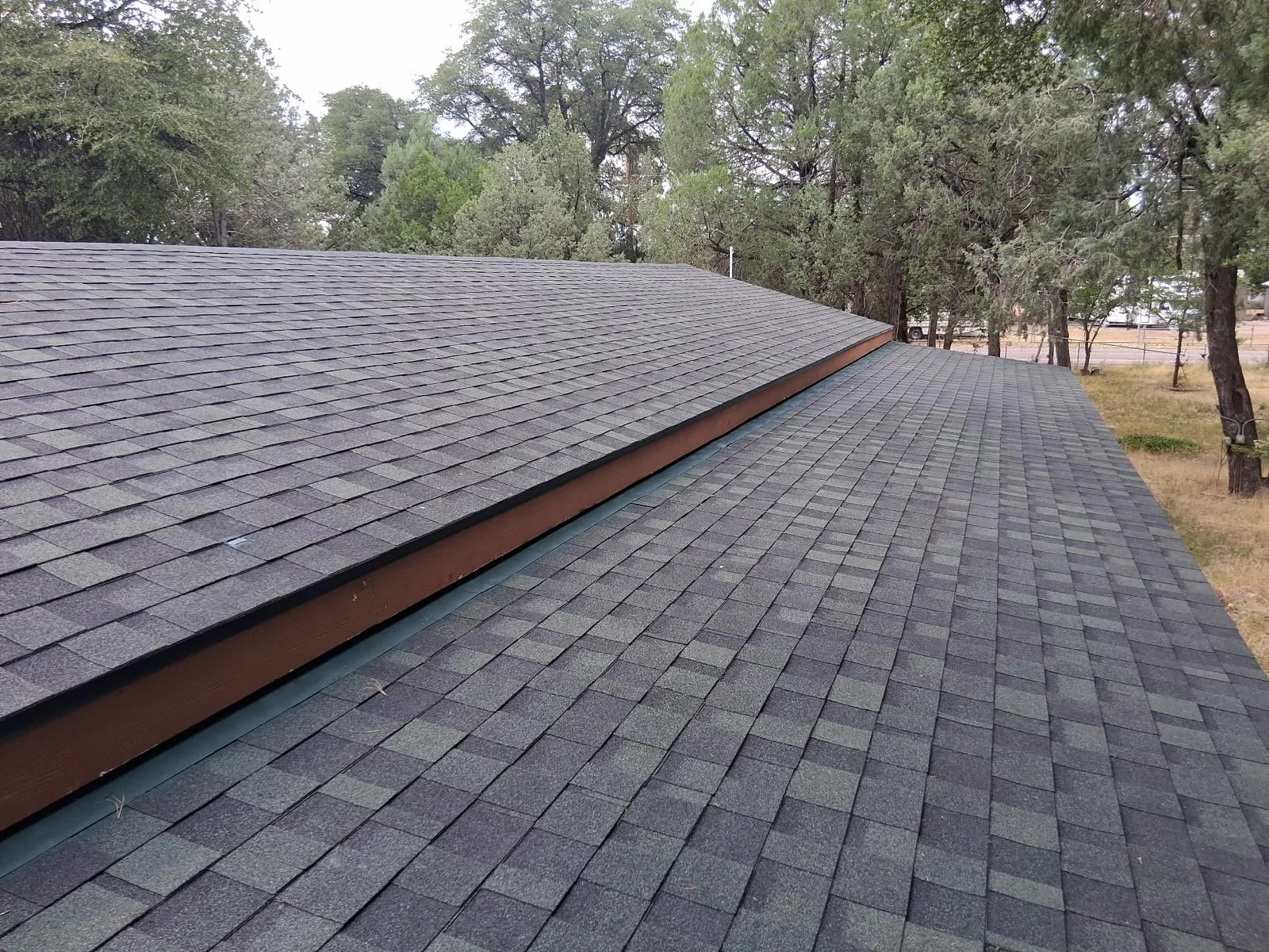 Two new shingle slopes meeting at a fascia line, with fresh drip edge and painted trim on a hillside home.