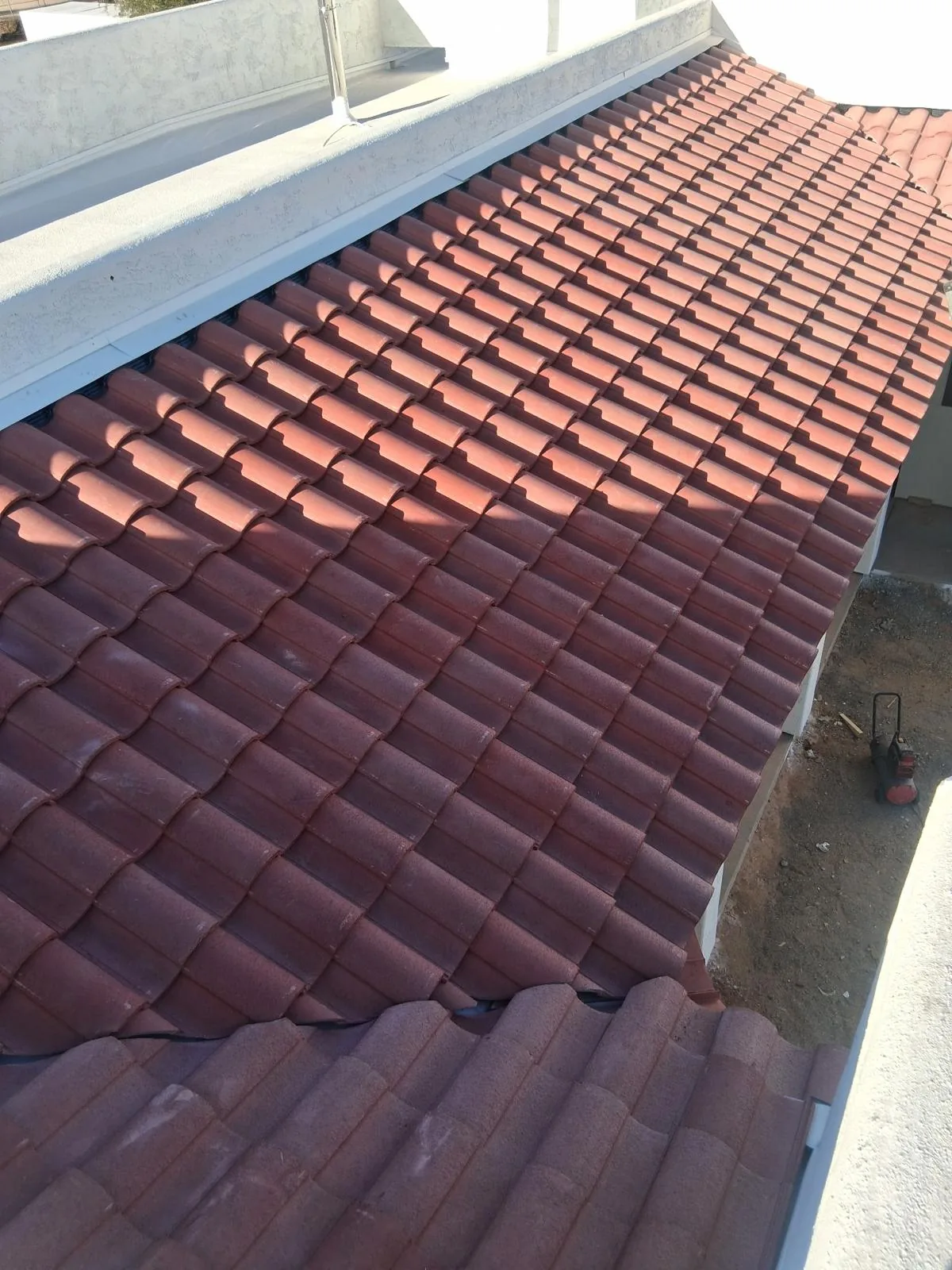 Red barrel tile laid in tight courses beside a coated parapet wall on a new-construction house.