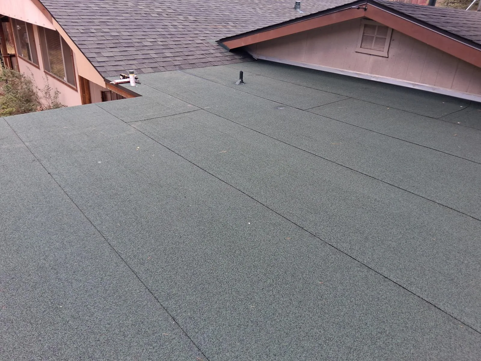 Low-slope section covered in granulated cap sheet where it tucks between two shingled gables.
